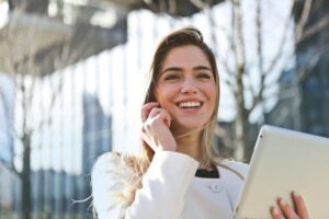 Best Times to Look For a Job - Smiling Woman on Cell Phone Holding Tablet